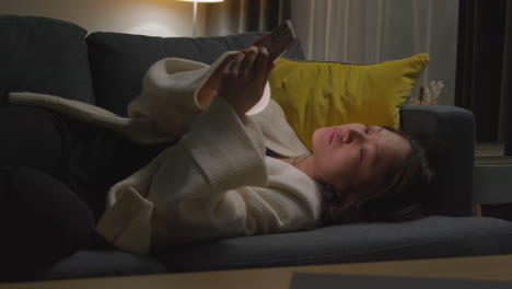 Woman-Spending-Evening-At-Home-Lying-On-Sofa-With-Mobile-Phone-Scrolling-Through-Internet-Or-Social-Media-5